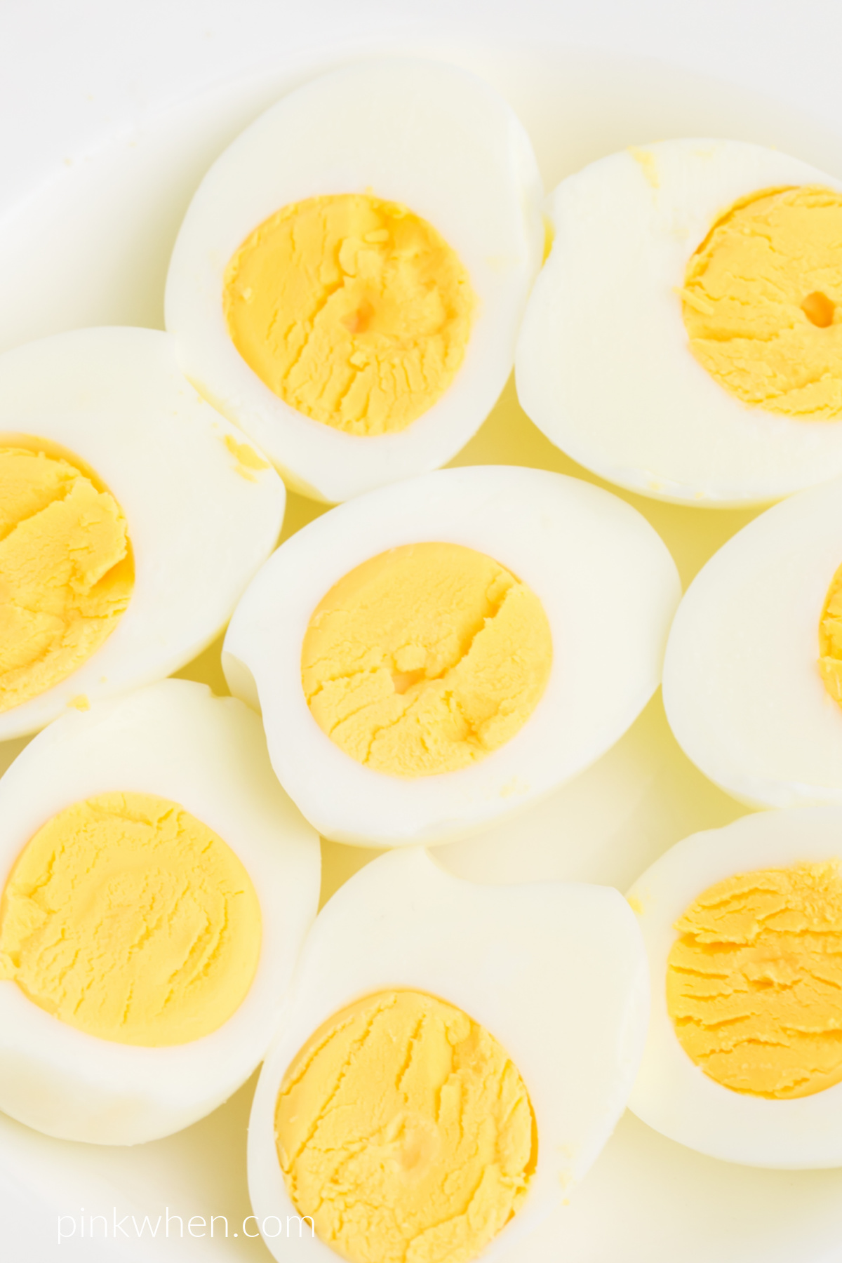 Close up photo of boiled eggs made in the air fryer that have been cut in half and are served on a white plate.