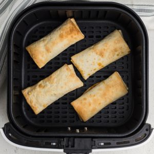 fully cooked frozen burritos in air fryer basket.