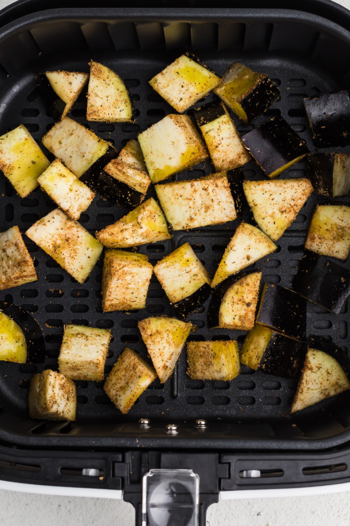 Seasoned eggplant wedges in a single layer in the prepared basket of the air fryer.