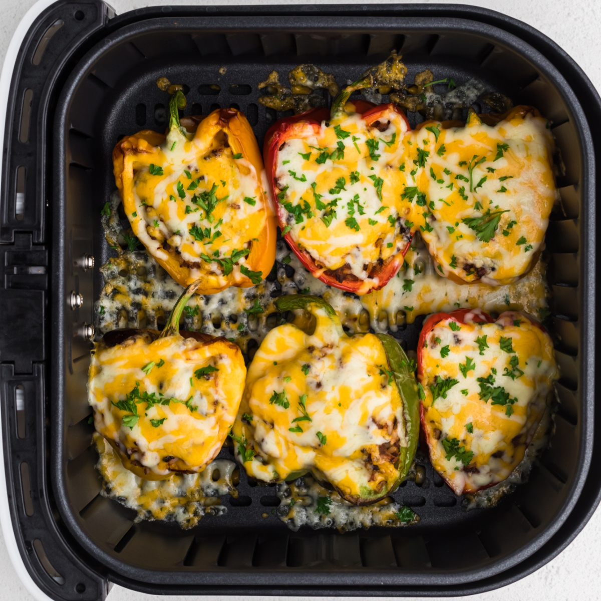 Stuffed peppers in the basket of the air fryer covered in cheese and topped with fresh parsley.
