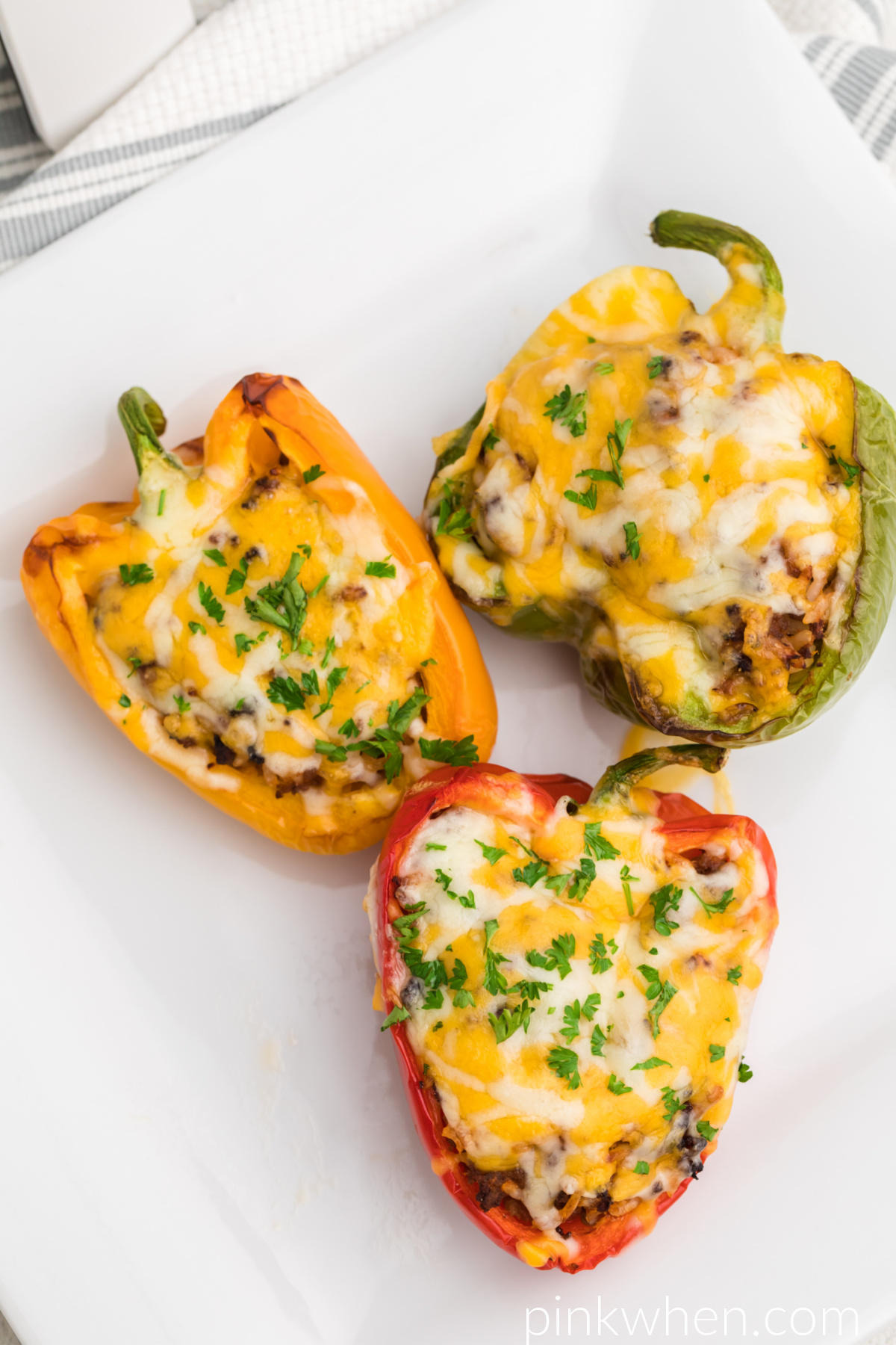 Green, yellow, and red stuffed peppers on a white plate ready to eat. 