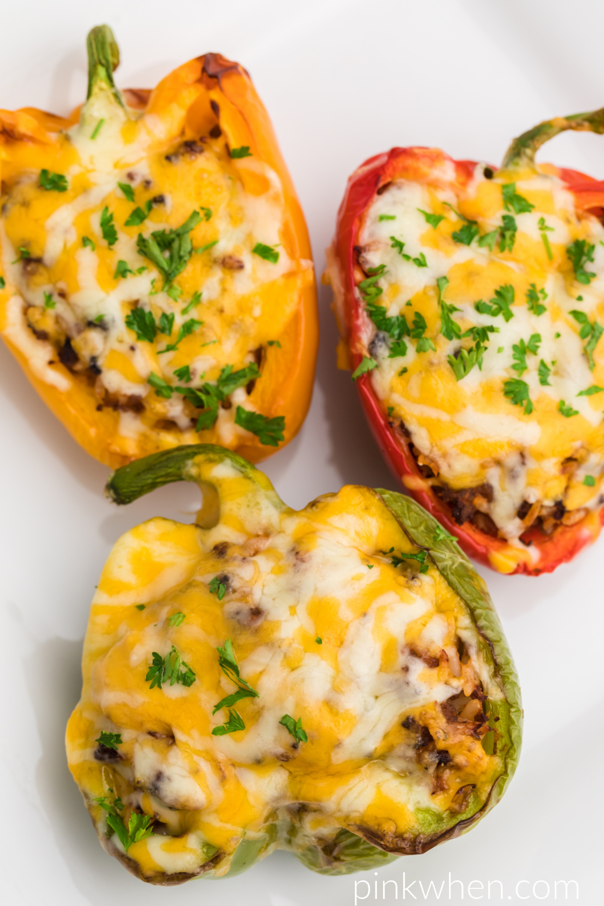 Stuffed peppers topped with cheese and fresh parsley served on a white plate and ready to eat. 