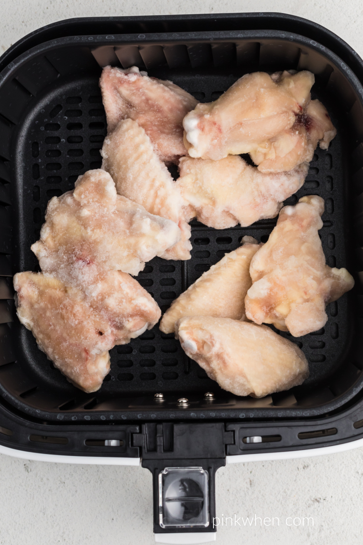 Naked frozen chicken wings in the basket of the air fryer.