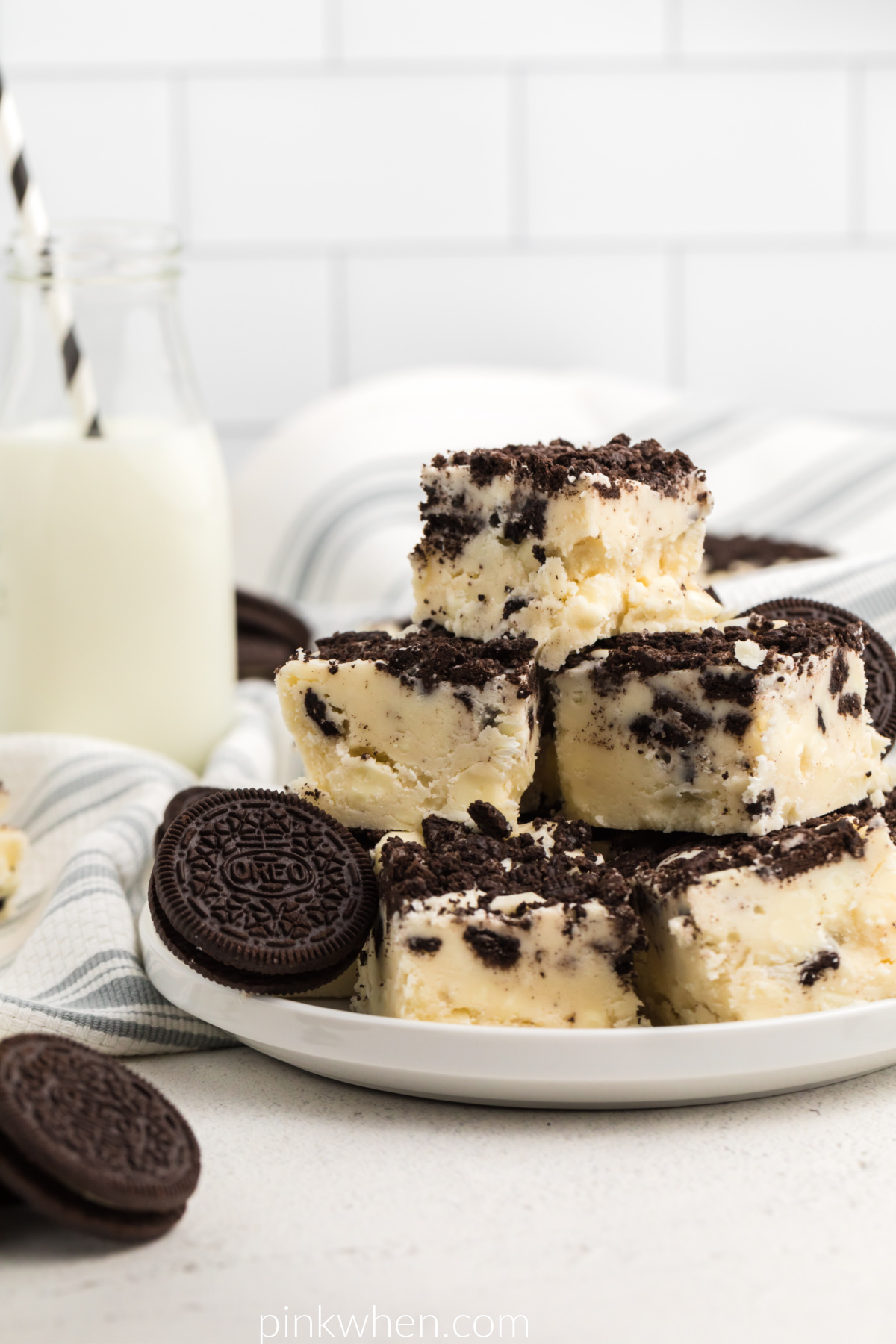 White Chocolate OREO fudge on a white plate with a glass of milk in the background. 