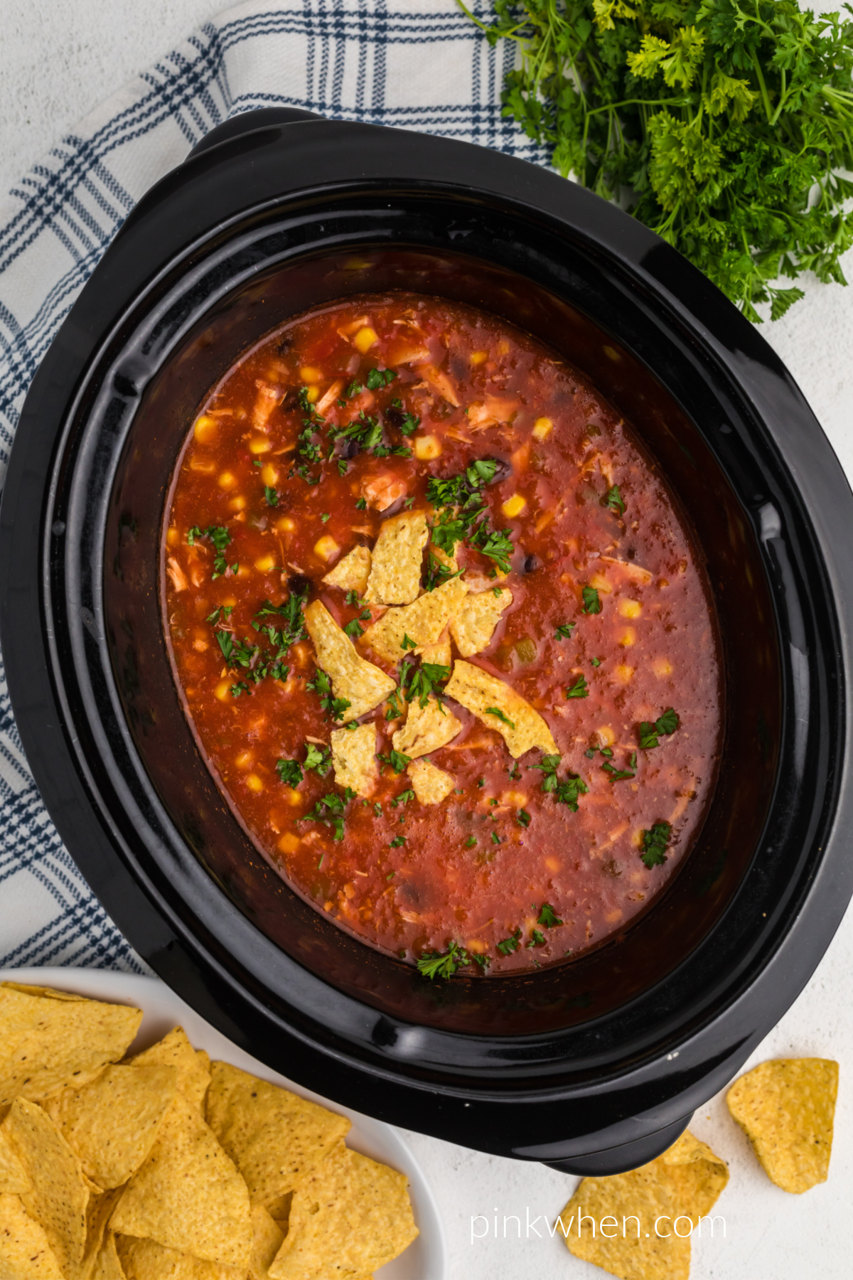 Southwestern Slow Cooker Chicken Tortilla Soup with crushed tortilla chips and fresh cilantro in the crock pot. 