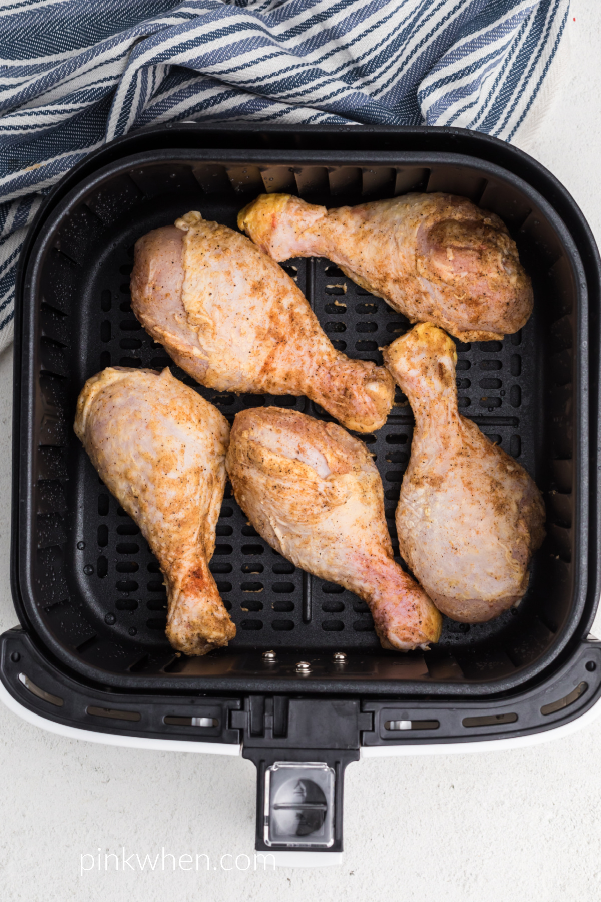 Seasoned chicken drumsticks in a single layer in the air fryer basket ready to be cooked.