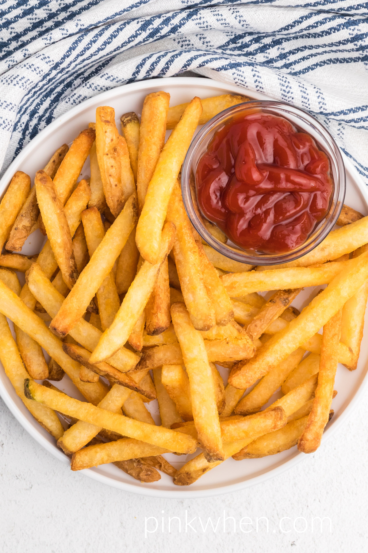 Fully cooked french fries that were cooked from frozen in an air fryer, on a white plate with a side of ketchup.