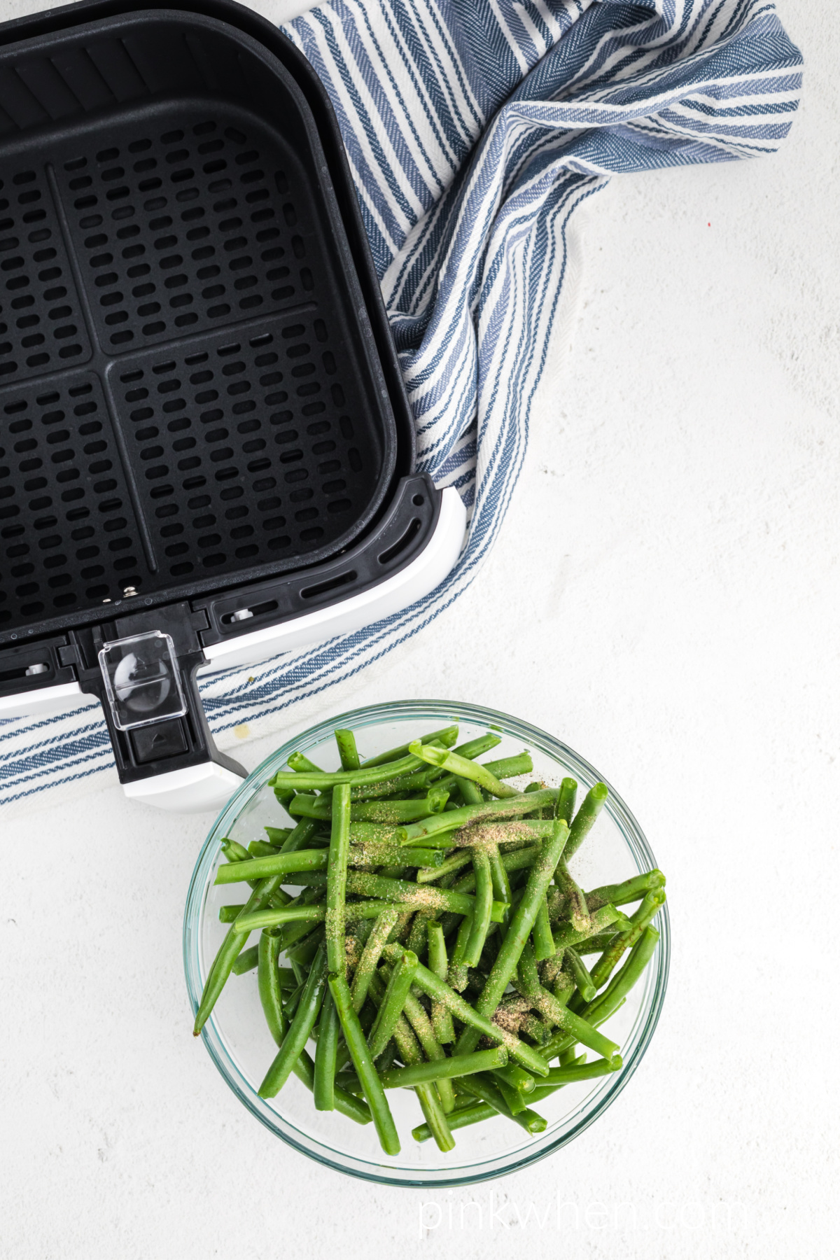 Fresh green beans covered in oil and seasonings and ready to be placed in the air fryer. 
