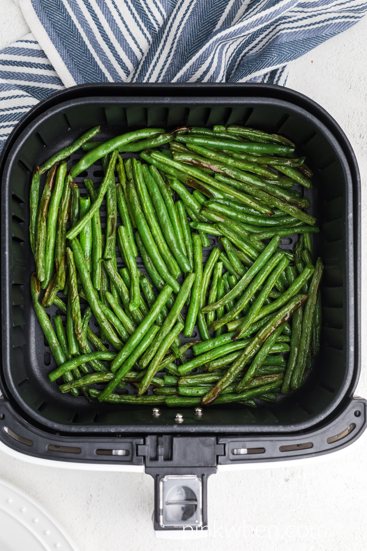 Fully cooked fried green beans in air fryer basket. 