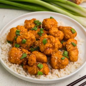 Orange chicken on a white plate served over rice.