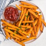 overhead photo of sweet potato fries made from frozen in the air fryer and served on a white plate with a side of ketchup.