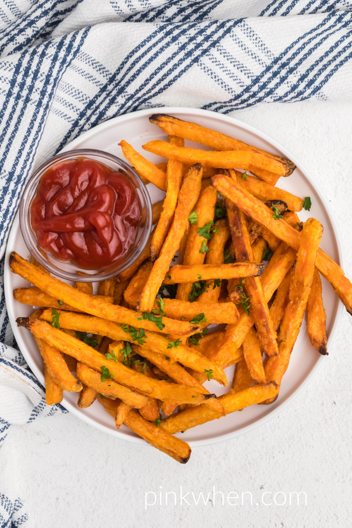 Frozen air fryer sweet potato fries that have been cooked in the air fryer and are on a white plate with a side of ketchup.