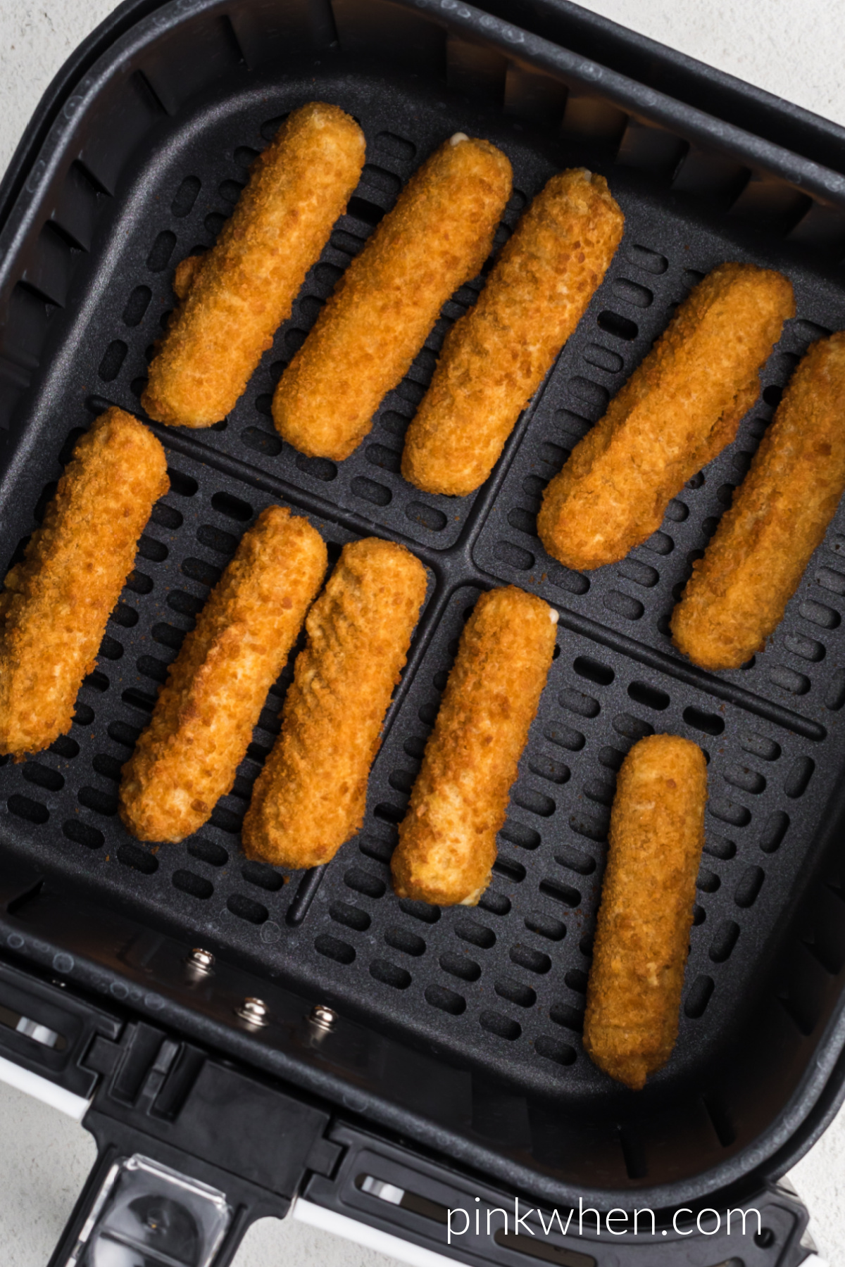 Air fried mozzarella sticks in the basket of the air fryer. 