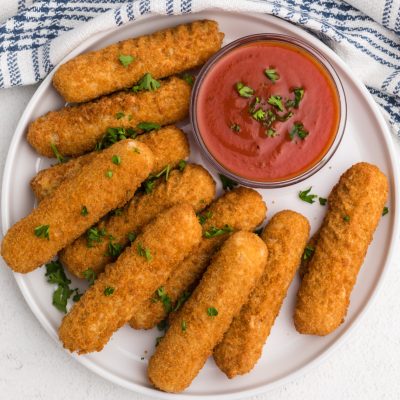 mozzarella sticks on a white plate with a side of dipping sauce.