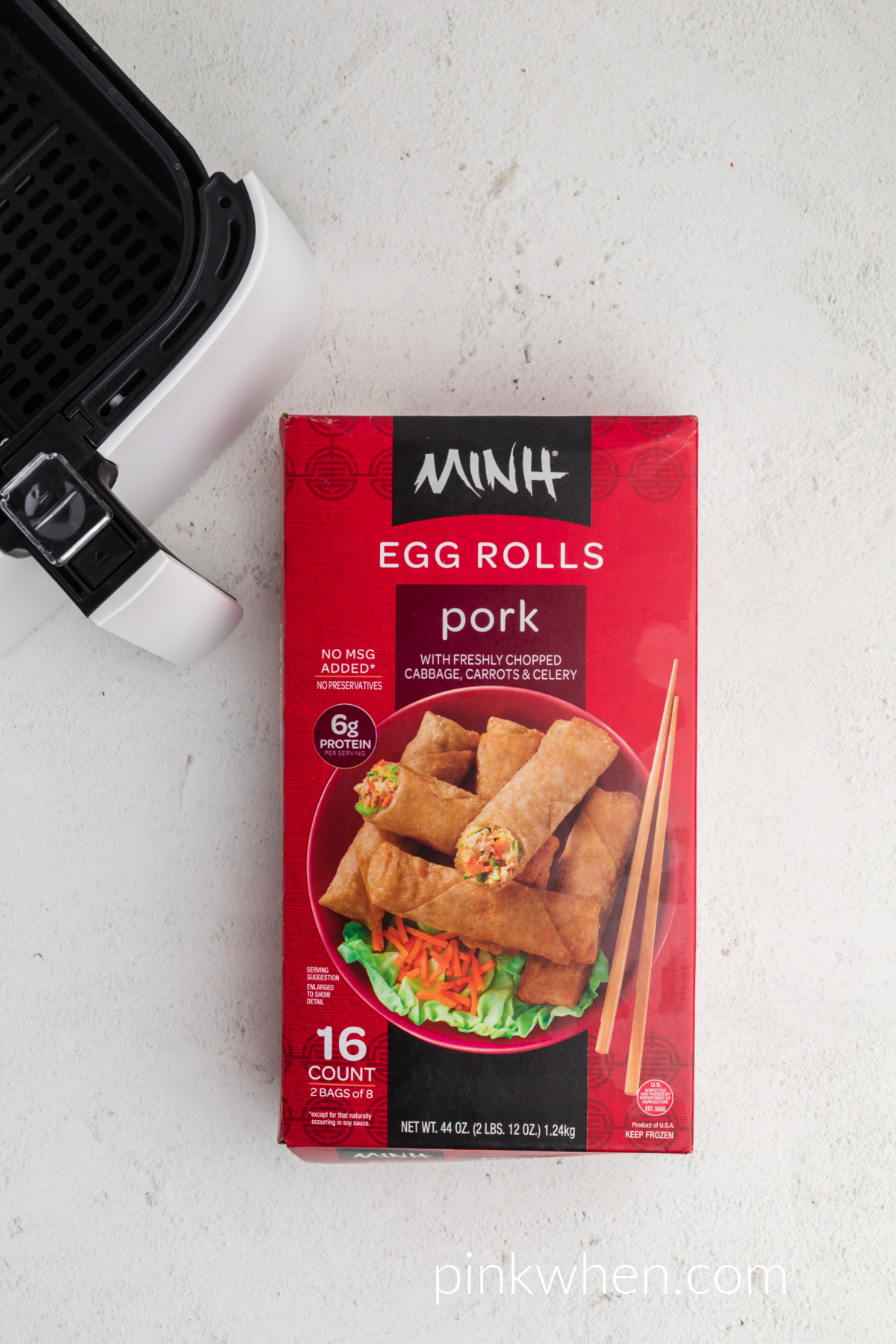 Box of frozen egg rolls next to the basket of the air fryer. 