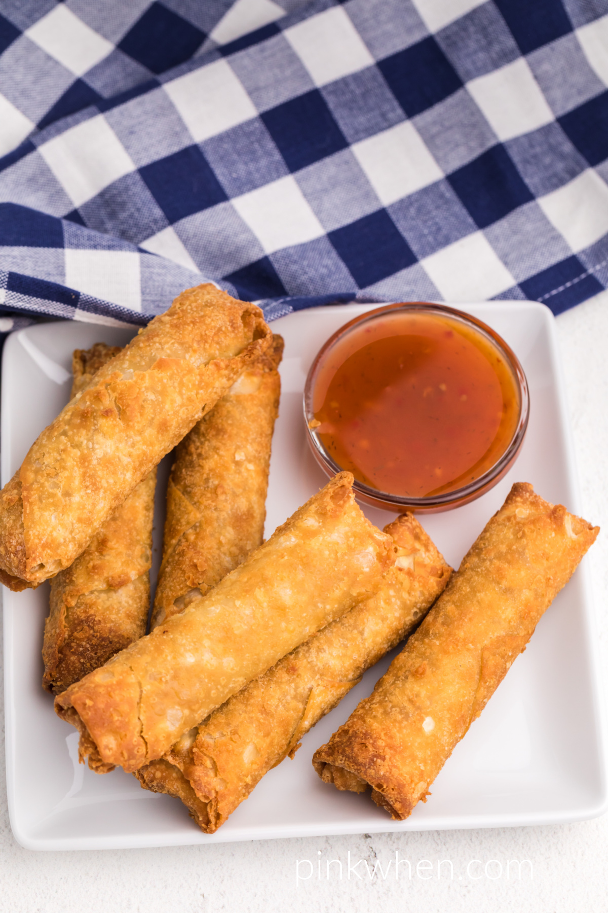 Frozen egg rolls made in the air fryer and served on a white plate with dipping sauce. 