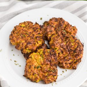Air fryer zucchini fritters on a white plate and sprinkled with fresh parsley.