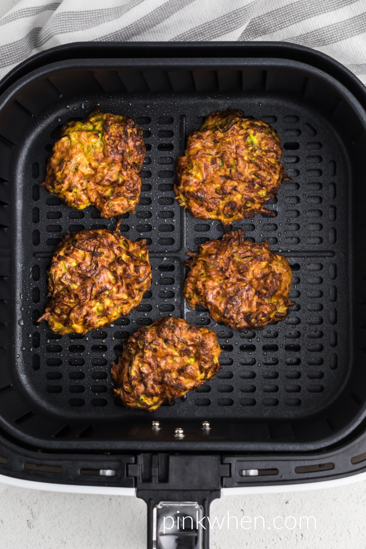 Air fryer zucchini fritters fully cooked and in the basket of the air fryer, ready to serve.