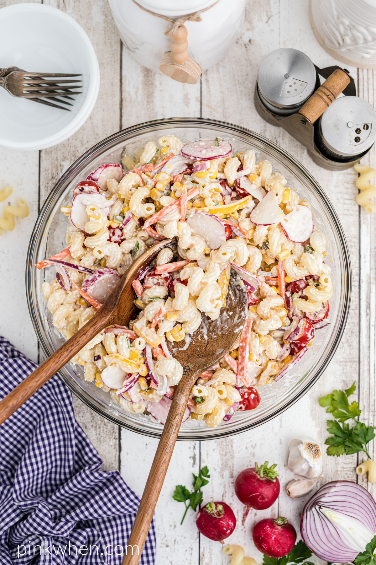 Overhead shot of summer pasta salad with wooden serving spoons, ready to serve.