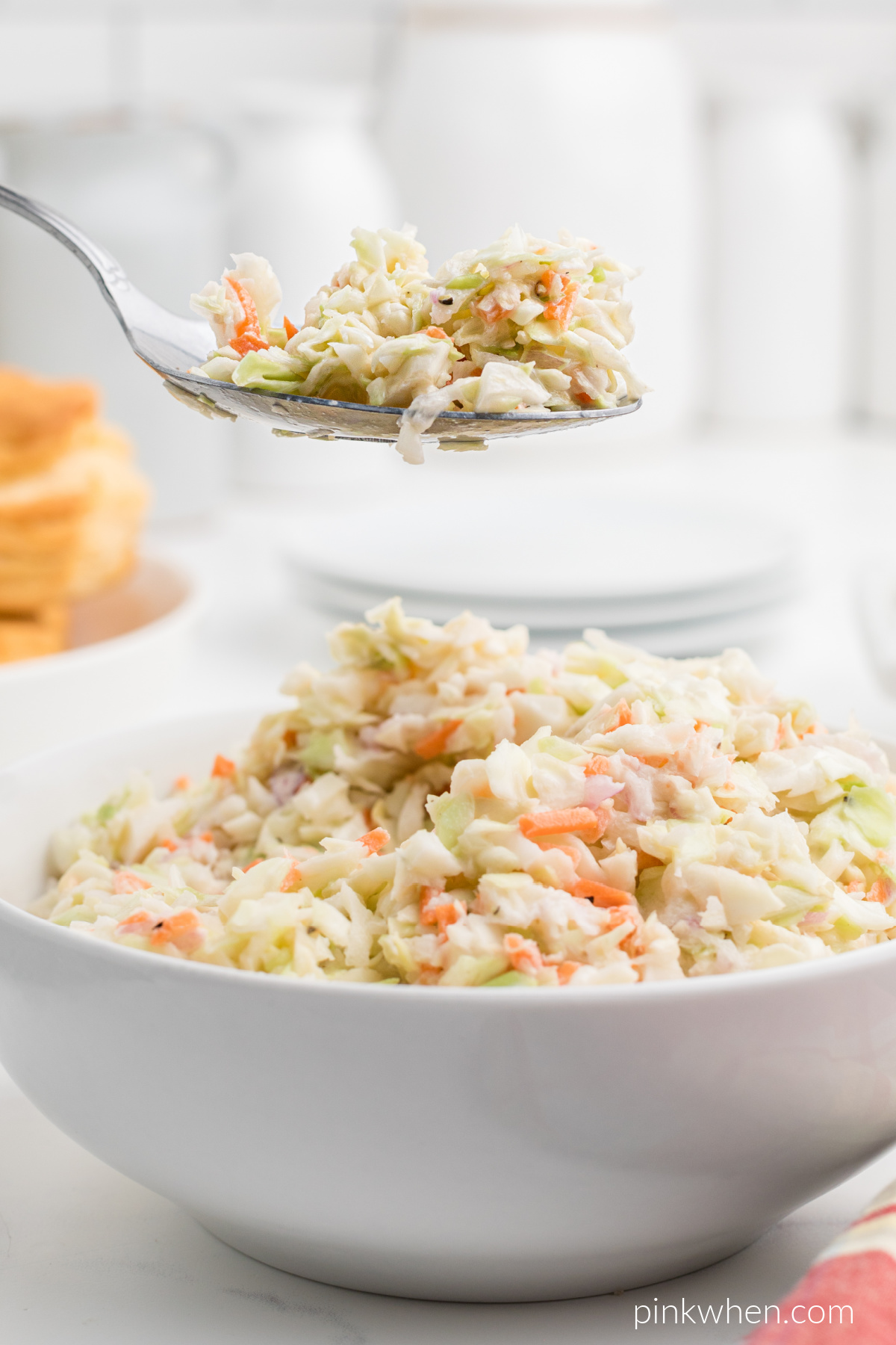 Bite shot of coleslaw on a spoon with a bowl of coleslaw underneath.