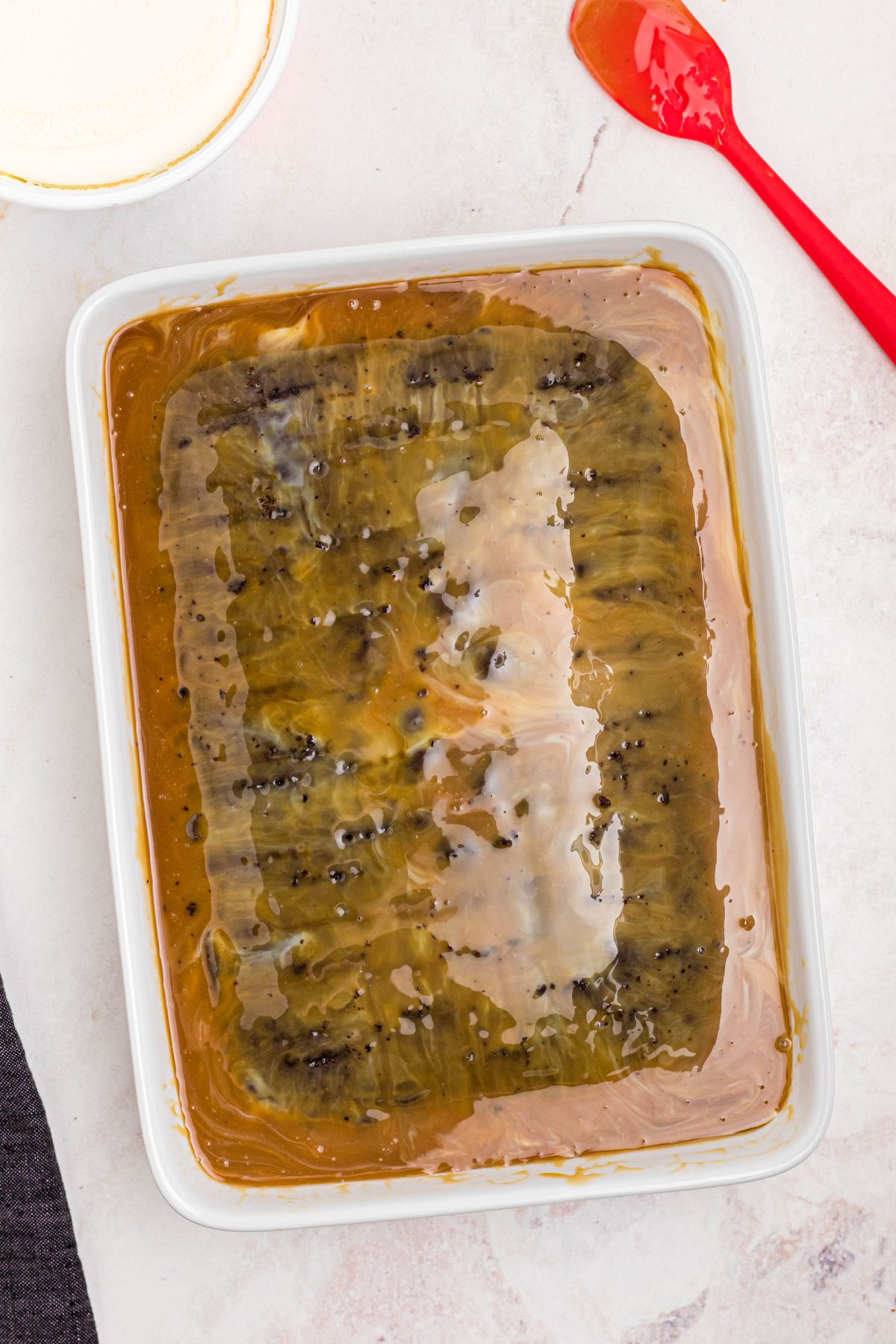 Caramel sauce poured over a baked cake in a rectangle white baking dish.