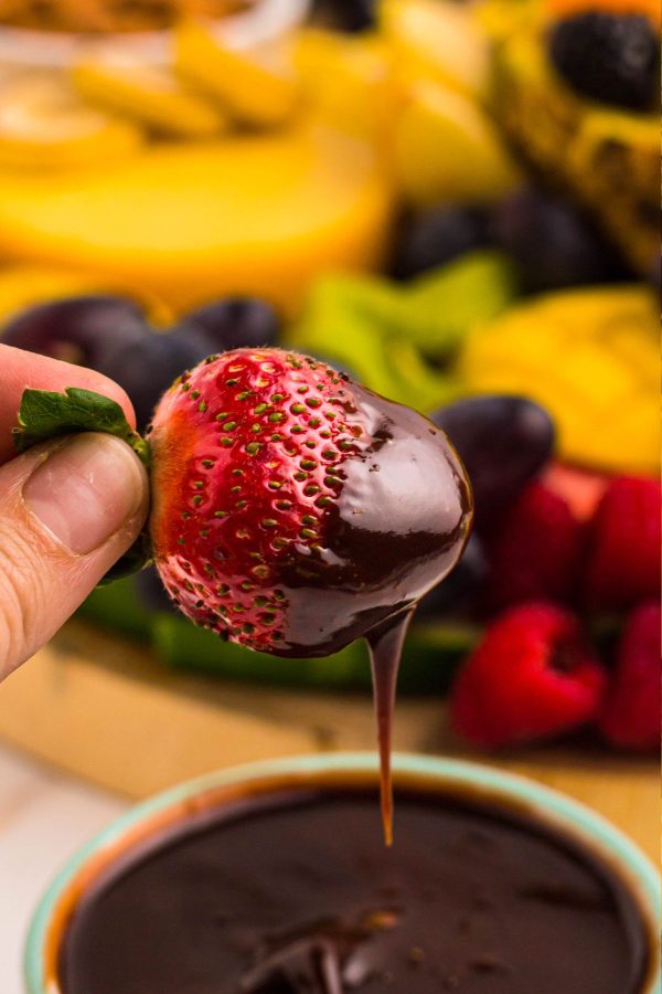 A hand holding a strawberry dipped in melted chocolate 