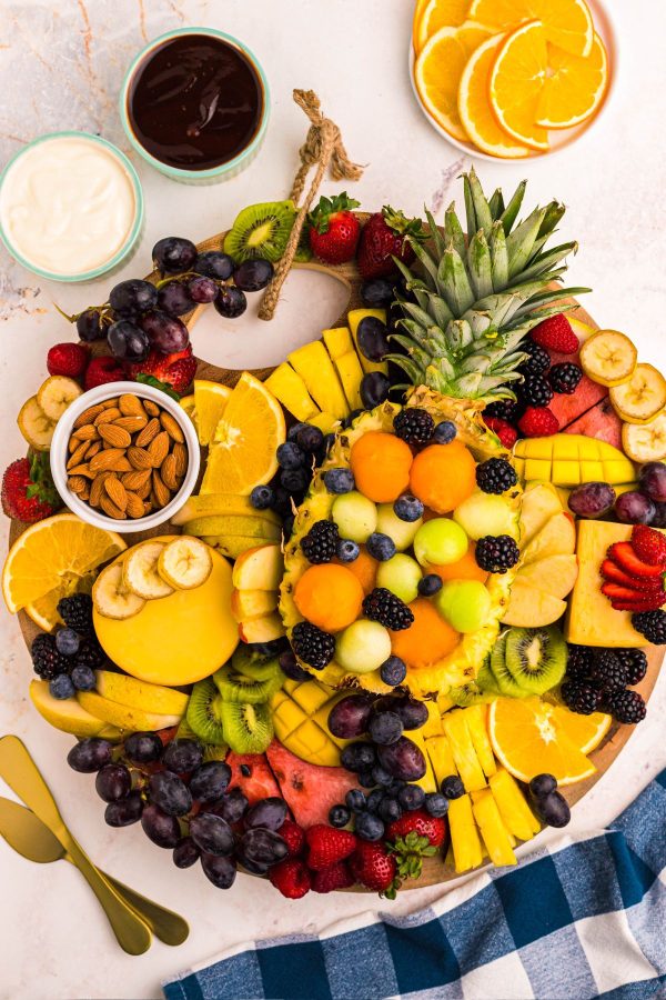 Various fruits sliced and fanned out on a wooden charcuterie board on a marble table. 
