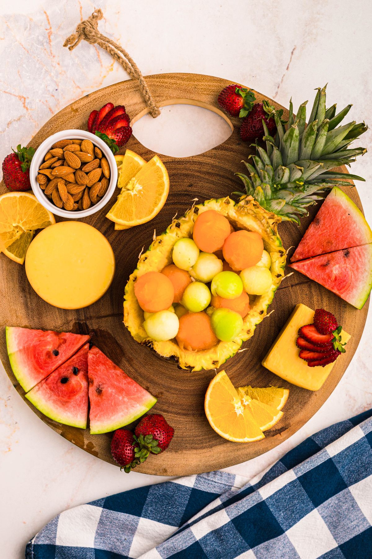 Large pieces of fruits like watermelon and emptied pineapple on a round charcuterie board.