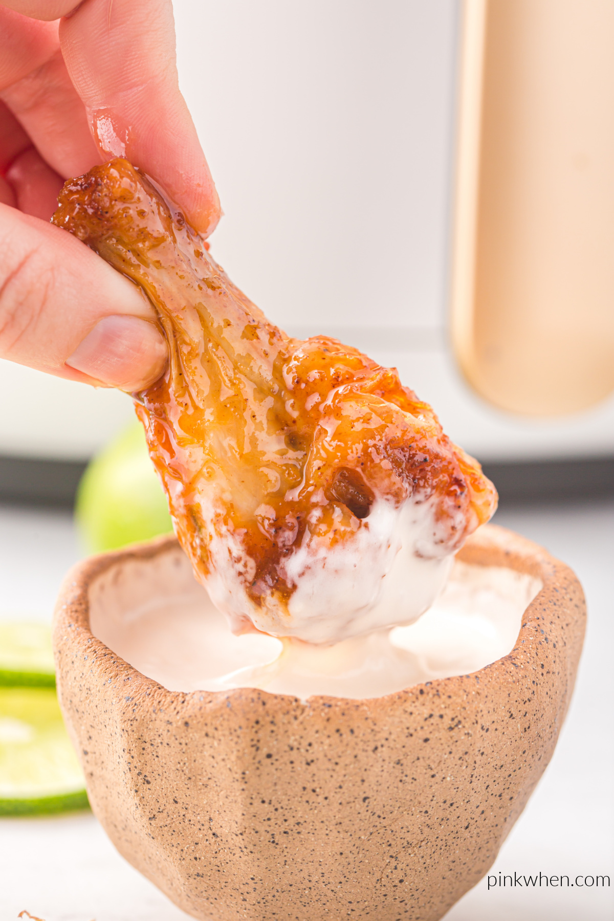 Honey sriracha wing being dipped into sauce. 