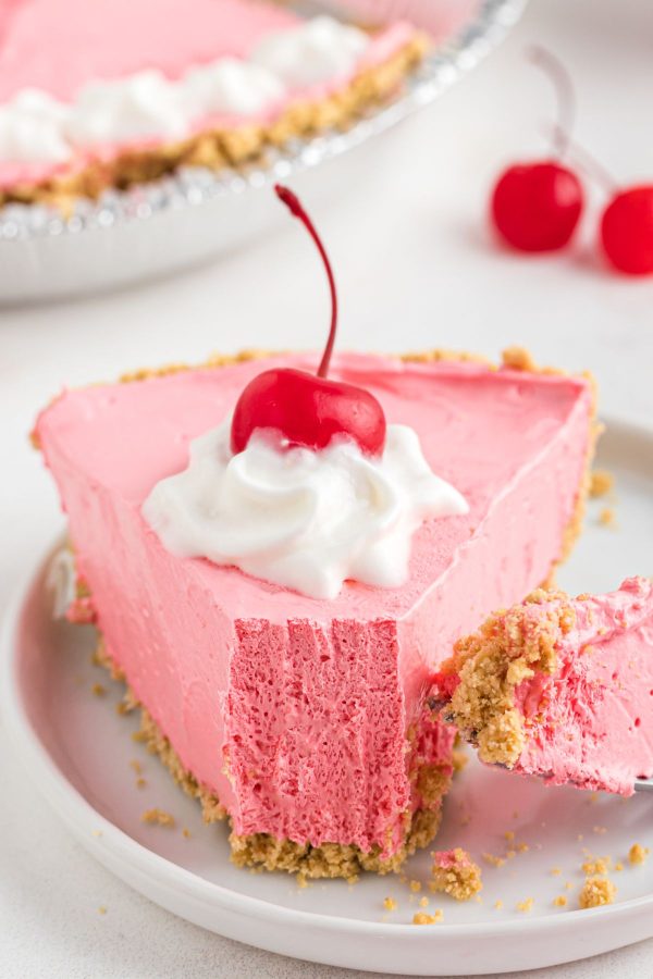 Slice of cherry kool aid pie on a small white plate with a fork taking a small piece.