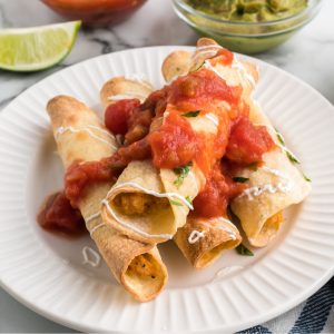 air fryer chicken taquitos on a white plate and topped with salsa and sour cream.