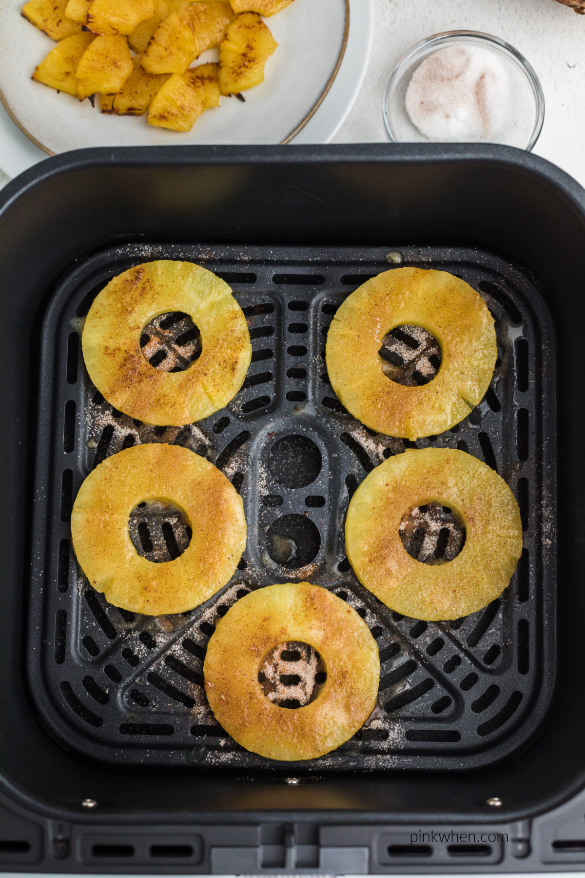 Pineapple rings sprinkled with cinnamon and sugar in the basket of the air fryer.