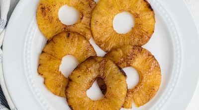 Air fryer pineapple rings topped with cinnamon and sugar and served on a white plate.