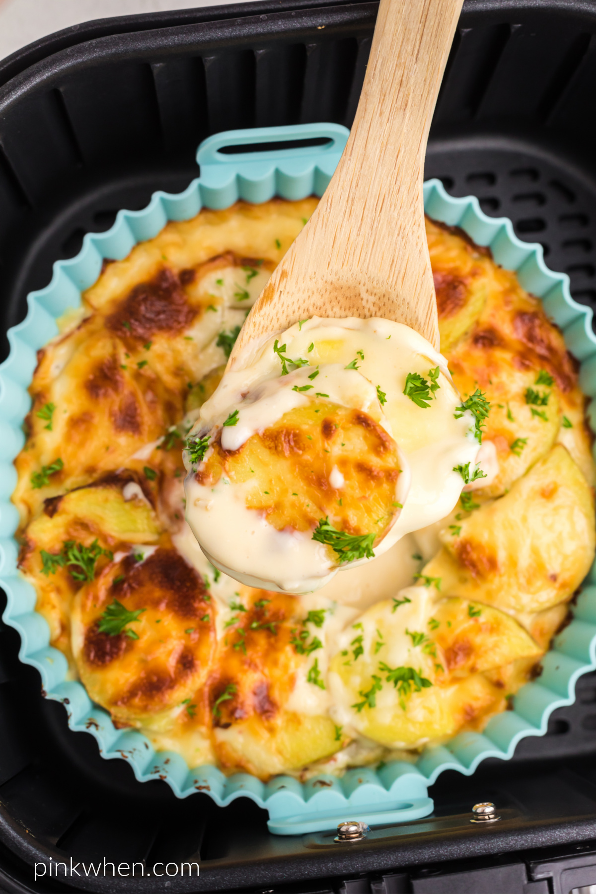 Cheesy scalloped potatoes in the air fryer, with a spoon scooping out a bite.