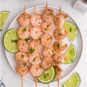 Overhead photos of shrimp skewers on a white plate with slices of lime.