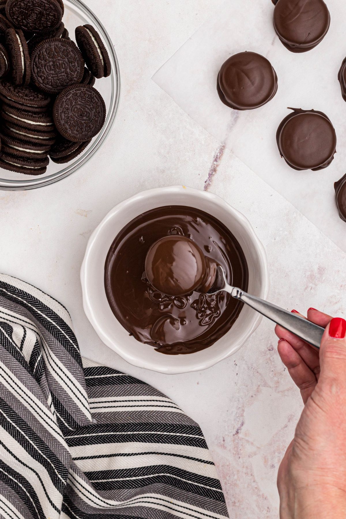 Oreo cookies being dipped in melted chocolate in a white bowl