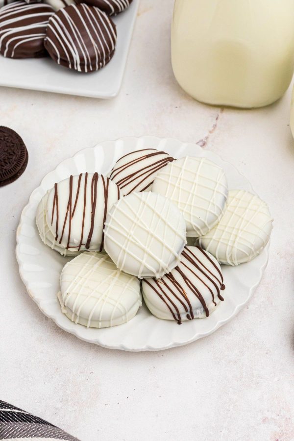 White chocolate covered Oreos stacked on a small white plate. 