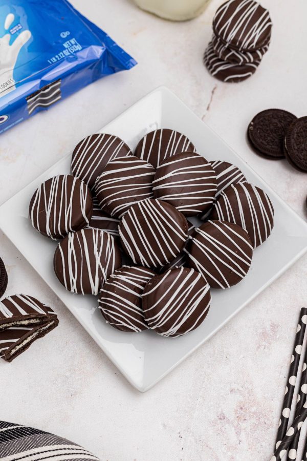 Chocolate covered Oreos stacked on a white square plate on a marble table. 
