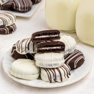 Chocolate covered Oreos stacked on a white plate in front of milk