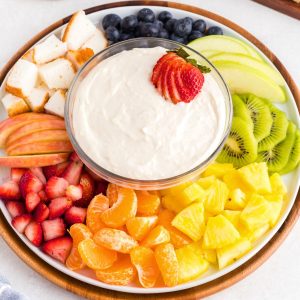 Creamy fruit dip in a clear bowl with fresh fruit surrounding the bowl.