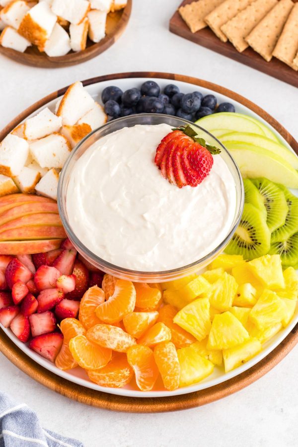 Fresh fruit and cake bread on a white platter with fruit dip in the center of the plate. 