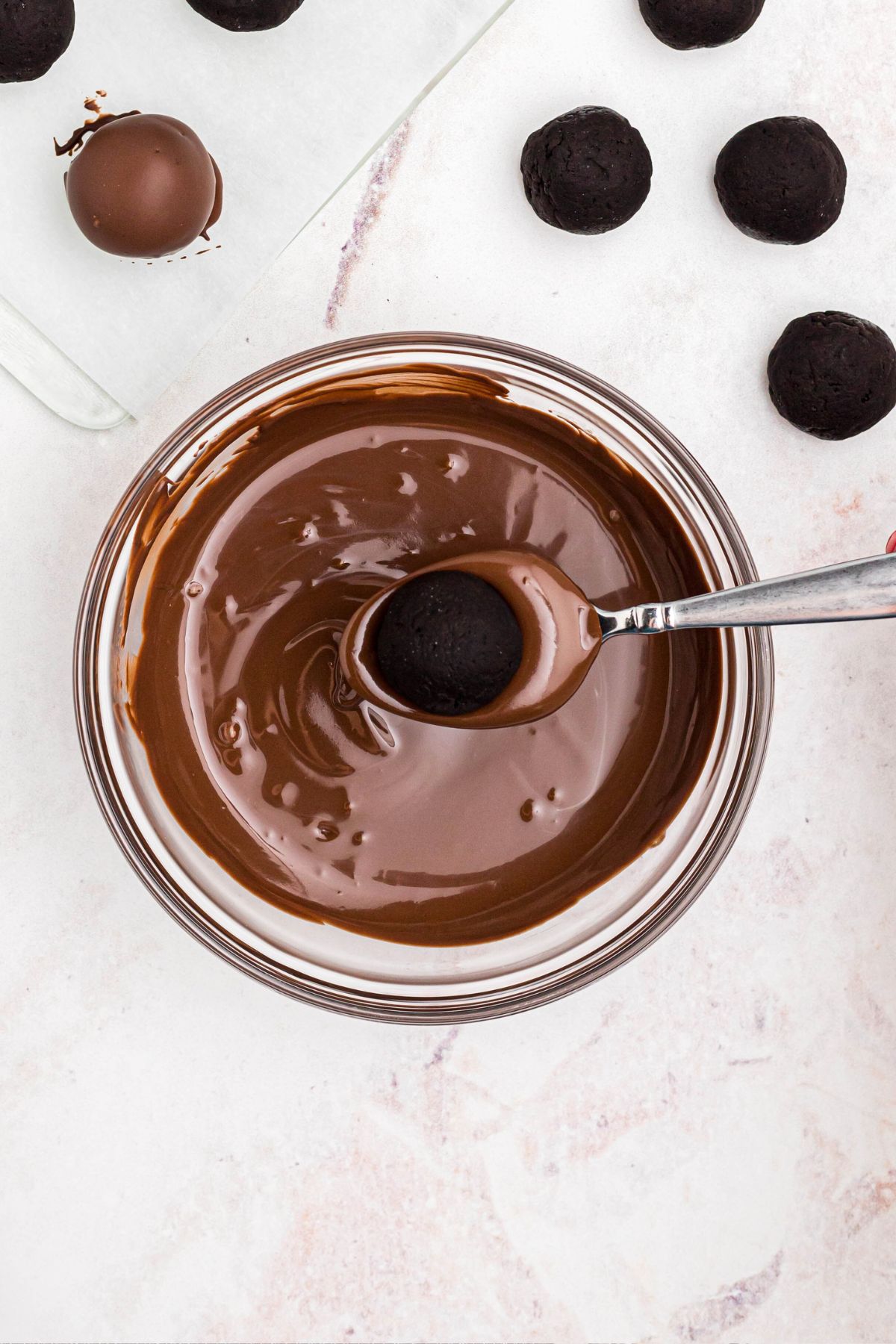 Oreo ball being dipped into melted chocolate in a clear glass bowl.