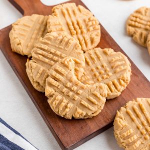 Golden peanut butter cookies on a dark cutting board with one cookie with a bite.
