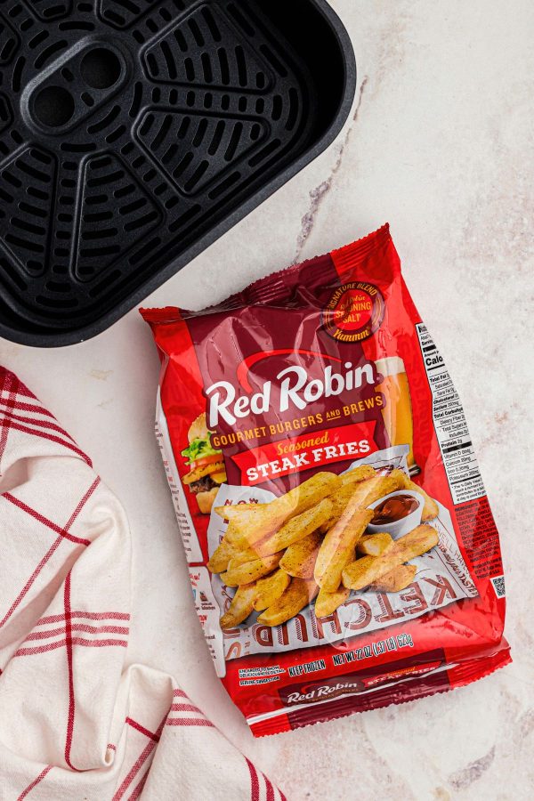 Bag of frozen red robin steak fries in front of air fryer basket. 