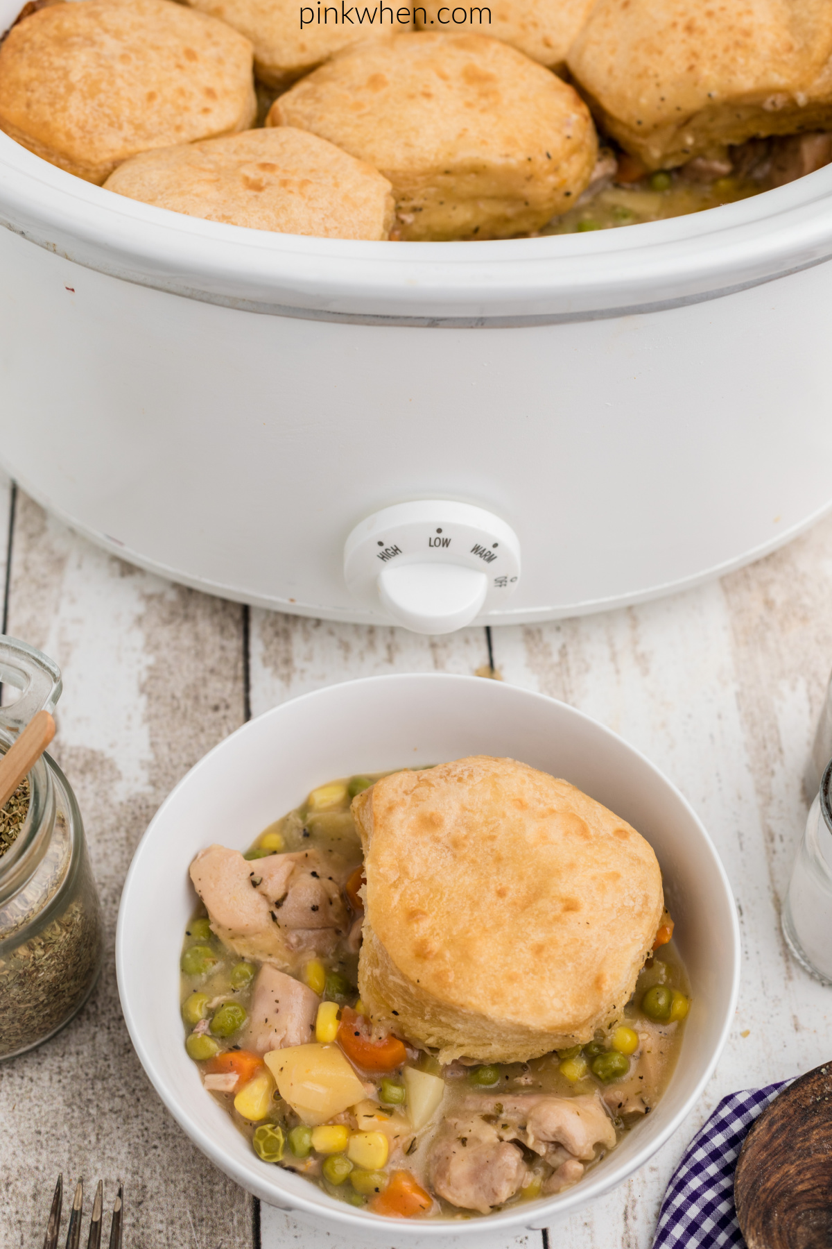 Chicken pot pie with biscuit topping in a bowl, with the slow cooker in the background.