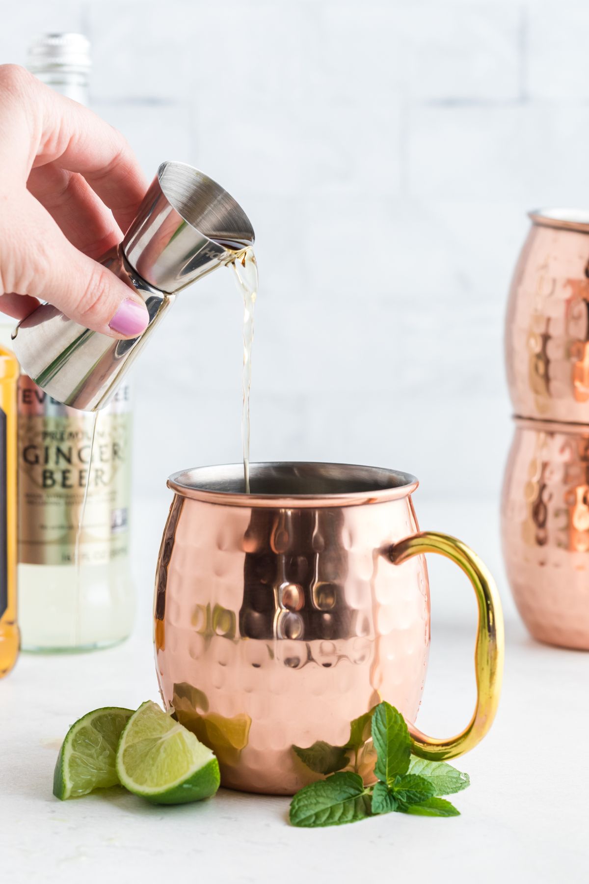 Copper mug being filled with whiskey with lime garnish on a marble table.