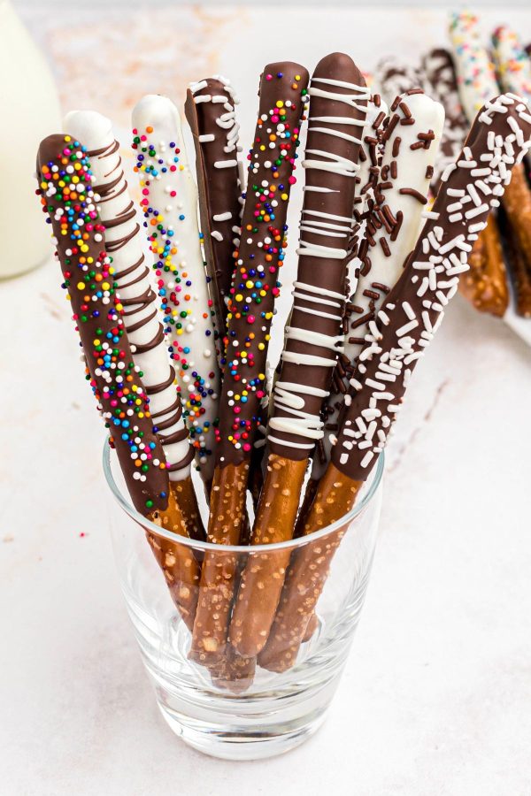 Chocolate and white chocolate coated pretzel rods stacked together in a clear glass.