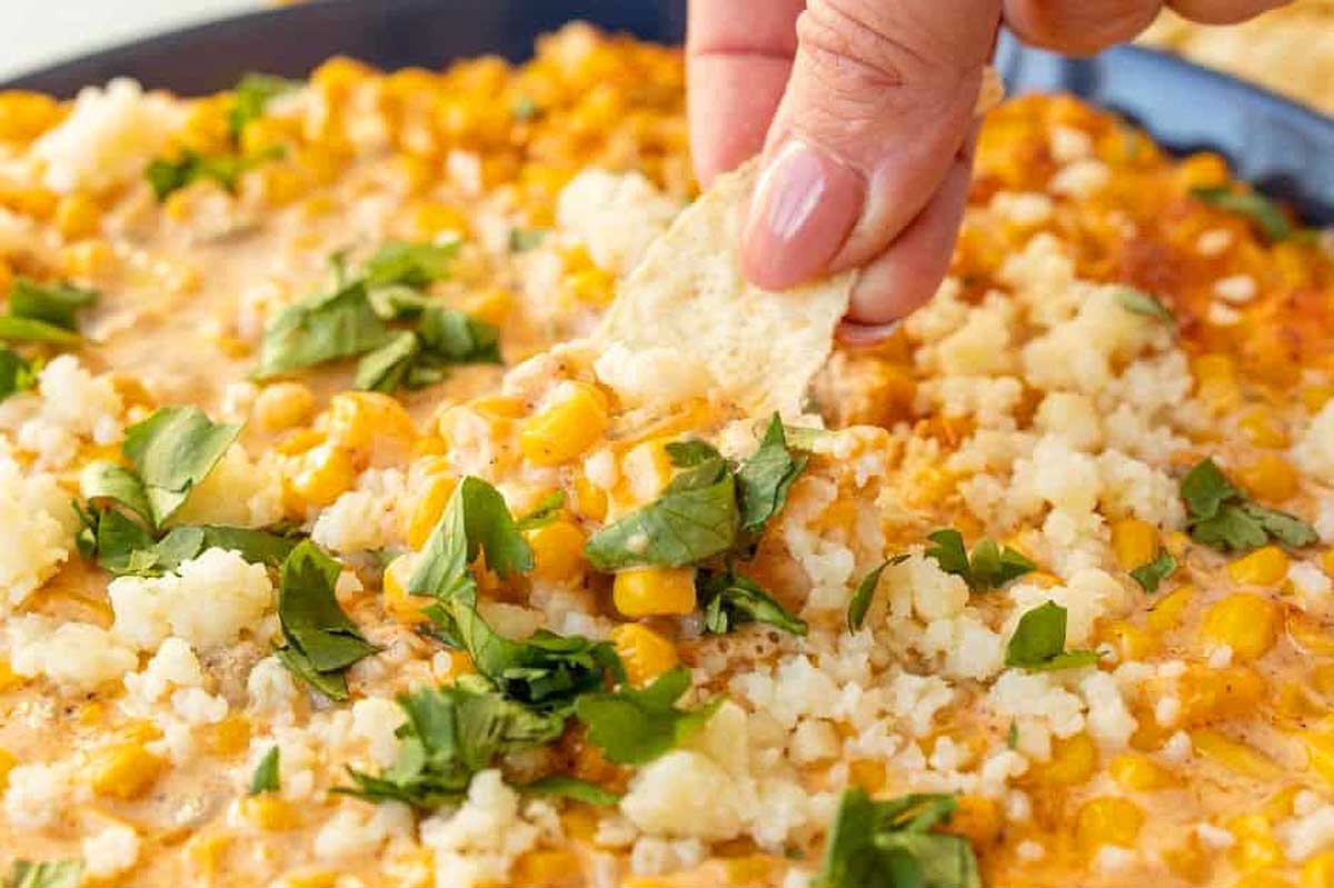 Air Fryer Mexican Corn dip with someone dipping a chip into it.