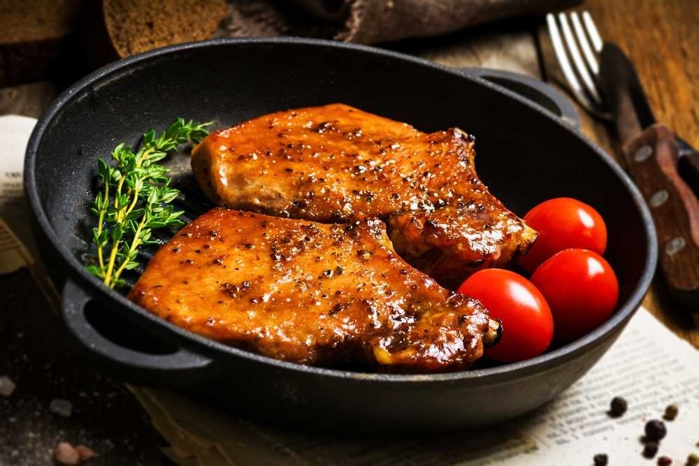 Pork chops in a skillet with tomatoes and fresh herbs.