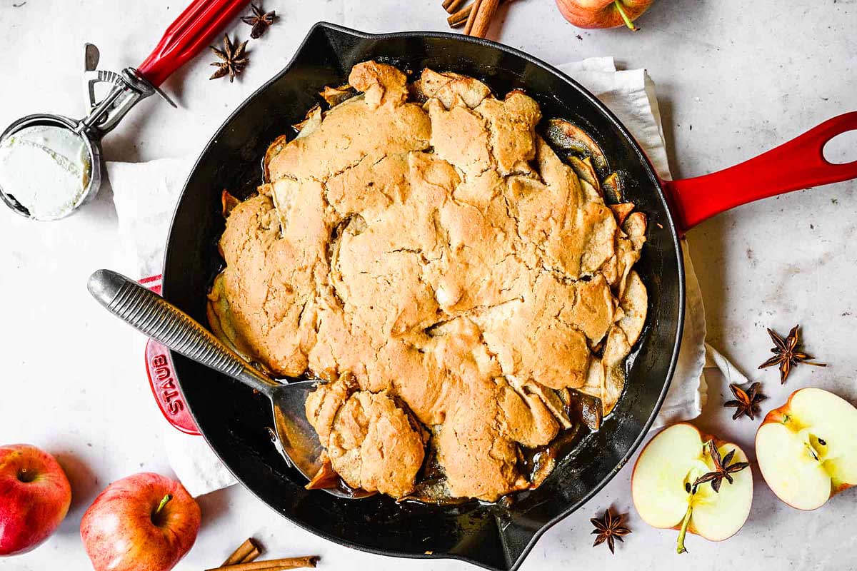 Apple cobbler in cast iron skillet with apples on the side.